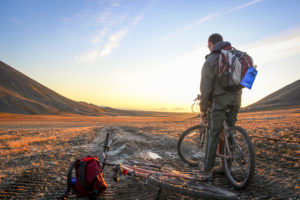 Man standing on a bike looking at the sunset over the mountains in the tundra in canada's high arctic in alert nunavut