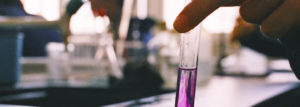 close up of holding a test tube with a pink substance in a lab